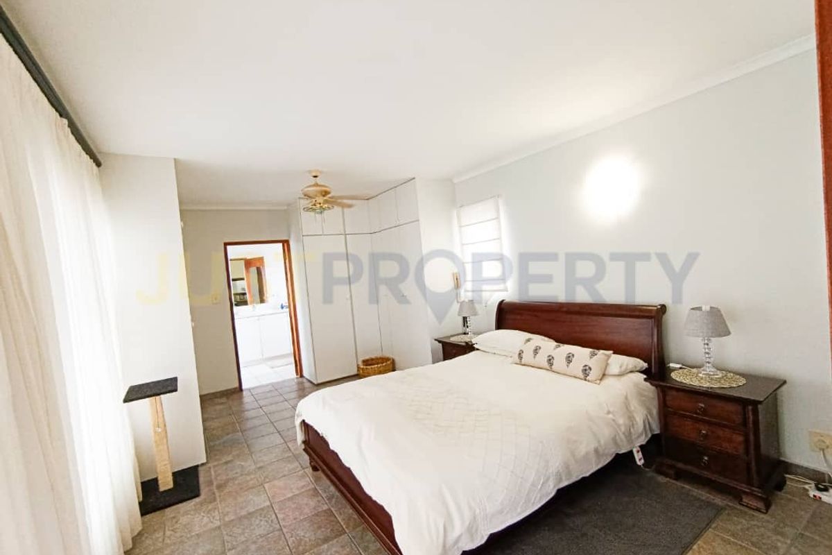 Spacious bedroom featuring tiled flooring, built-in cupboards, and a ceiling fan, offering a functional layout with direct access to an adjoining room.
