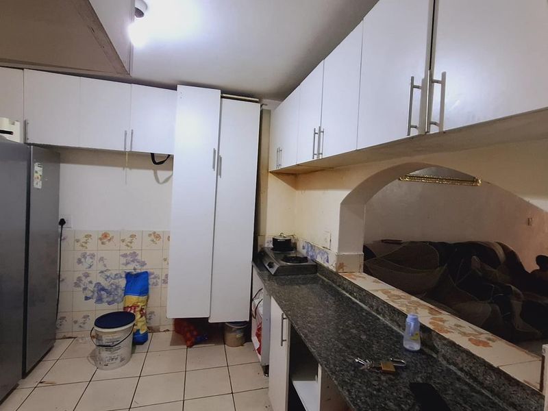 A functional kitchen featuring white built-in cabinetry, granite countertops, and a tiled backsplash, connected to the living area via a decorative archway.
