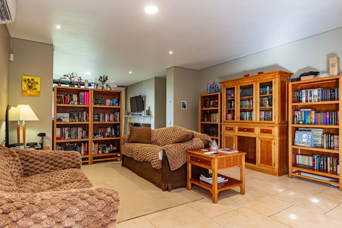 A spacious living room featuring neutral tiled flooring, recessed downlighting, and a wall-mounted split-system air conditioning unit.