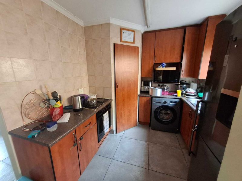 A functional kitchen featuring wood-finish cabinetry, tiled splashbacks, built-in oven and hob, and dedicated space for a washing machine.