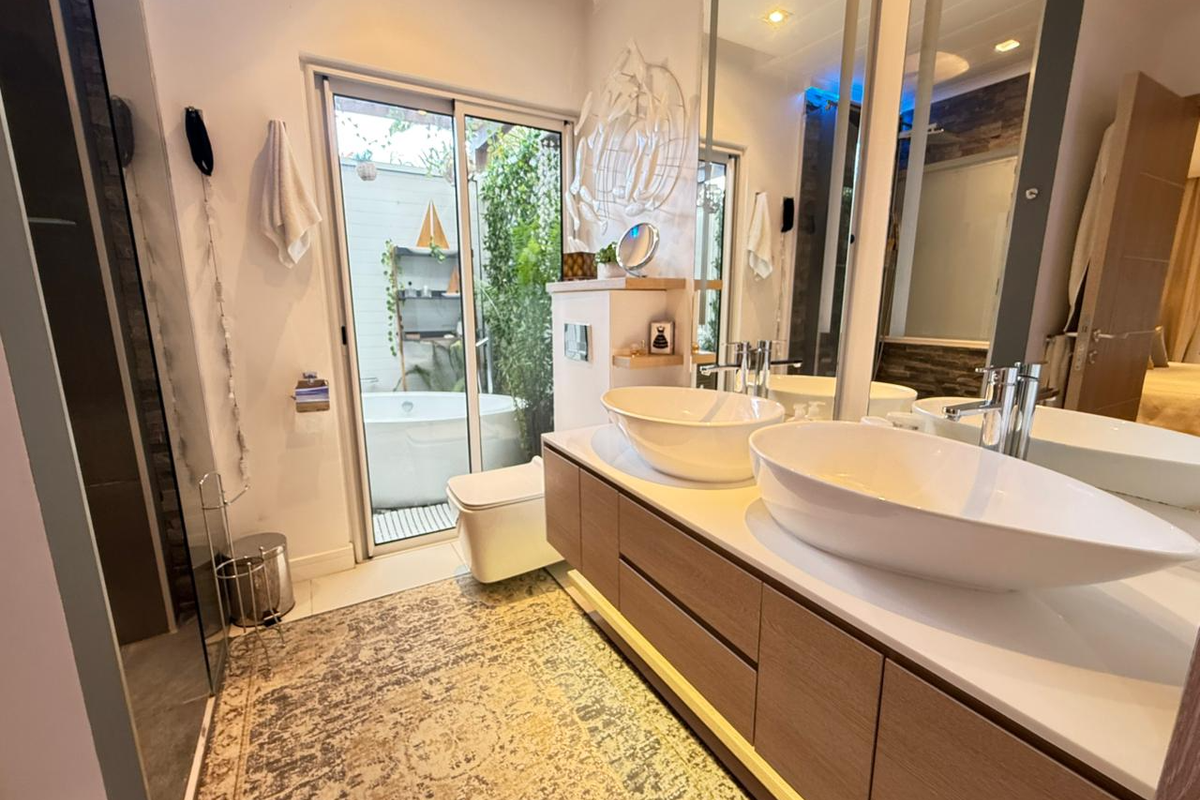 Modern bathroom featuring a double vanity with vessel sinks, sleek cabinetry, and a glass sliding door opening to a private outdoor area with a tub.