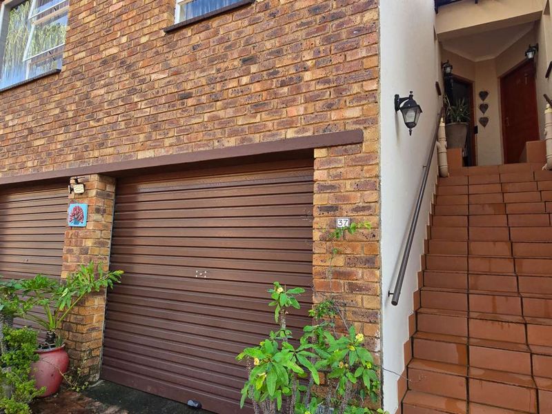 Front elevation of a townhouse featuring a face brick facade, integrated roller garage doors, and an external tiled staircase leading to the entrance.