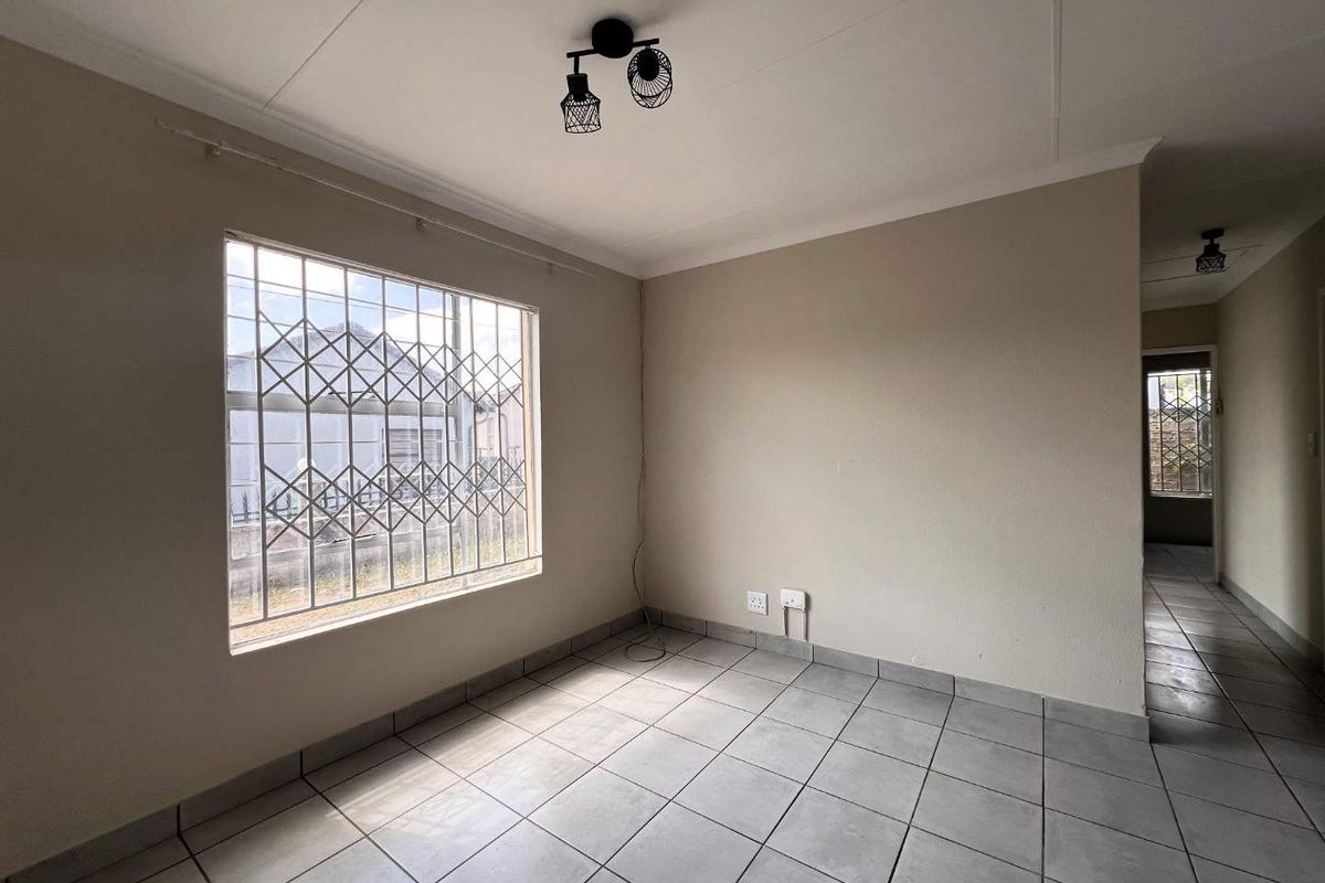 An empty living room featuring neutral walls, tiled flooring, and a window fitted with security bars.