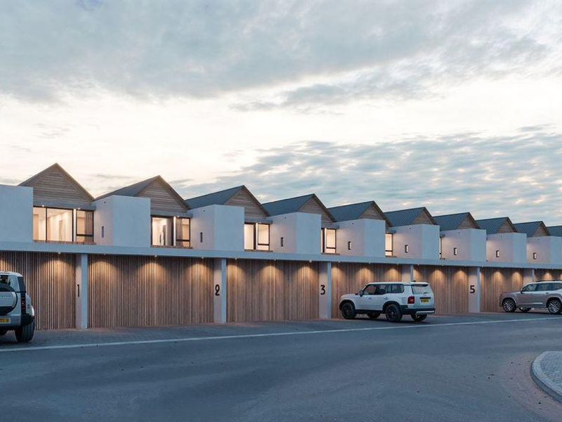 A modern row of townhouses featuring timber-clad garage doors, pitched roofs, and integrated exterior lighting, showcasing a contemporary architectural design.