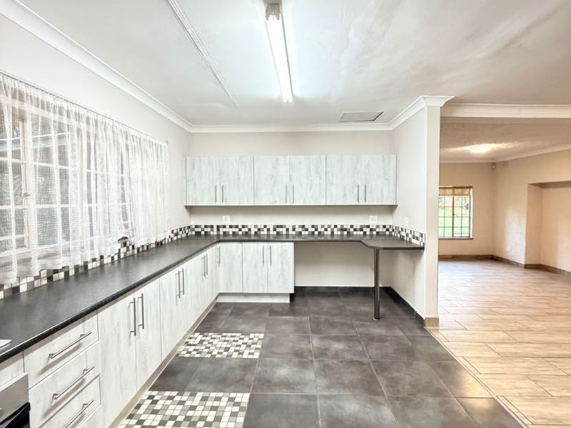 A spacious, empty kitchen featuring light-toned built-in cabinetry, dark laminate countertops, mosaic tile backsplash, and large format floor tiles.