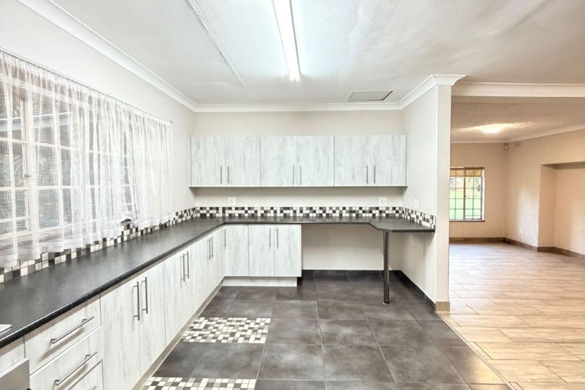 A spacious, empty kitchen featuring light-toned built-in cabinetry, dark laminate countertops, mosaic tile backsplash, and large format floor tiles.