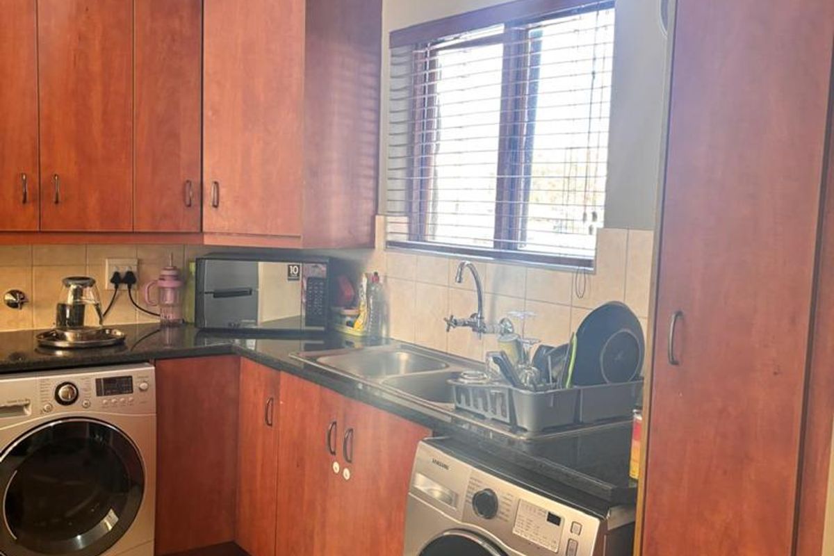 A functional kitchen featuring warm-toned laminate cabinetry, granite countertops, tiled flooring, and integrated space for laundry appliances.