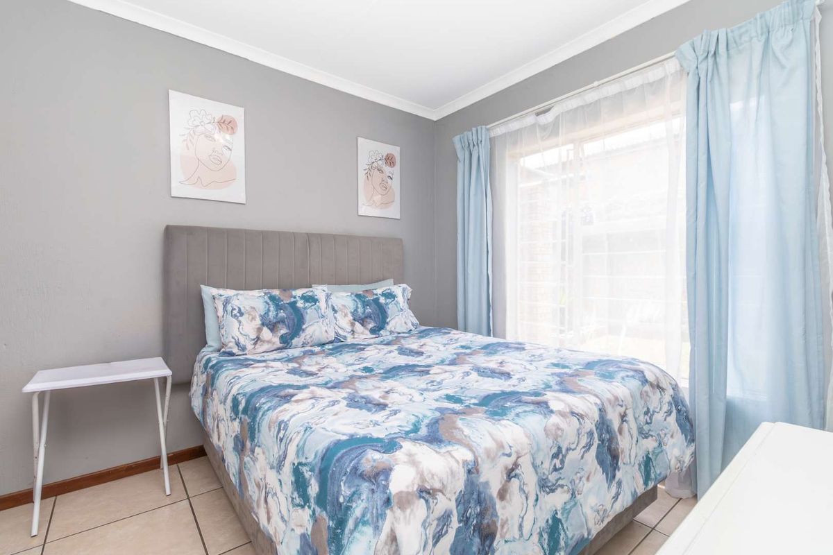 A well-maintained bedroom featuring neutral grey walls, tiled flooring, and a large window allowing for natural light.