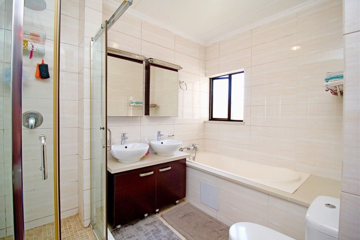 A well-maintained bathroom featuring a double vanity with vessel sinks, a built-in bathtub, and a separate glass-enclosed shower with full-height wall tiling.