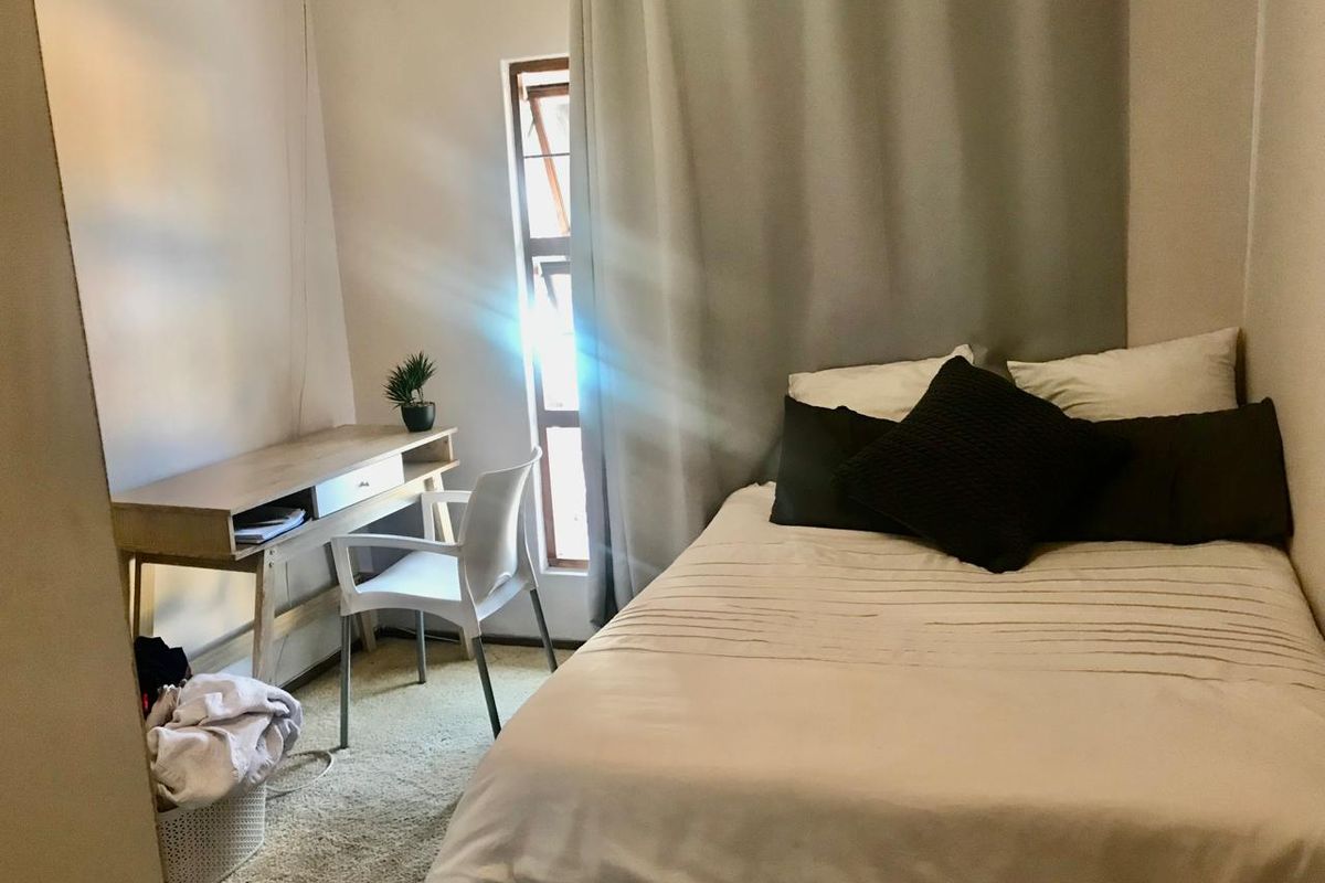 A compact bedroom featuring carpeted flooring and a window with floor-to-ceiling curtains, providing a functional and cozy sleeping space.