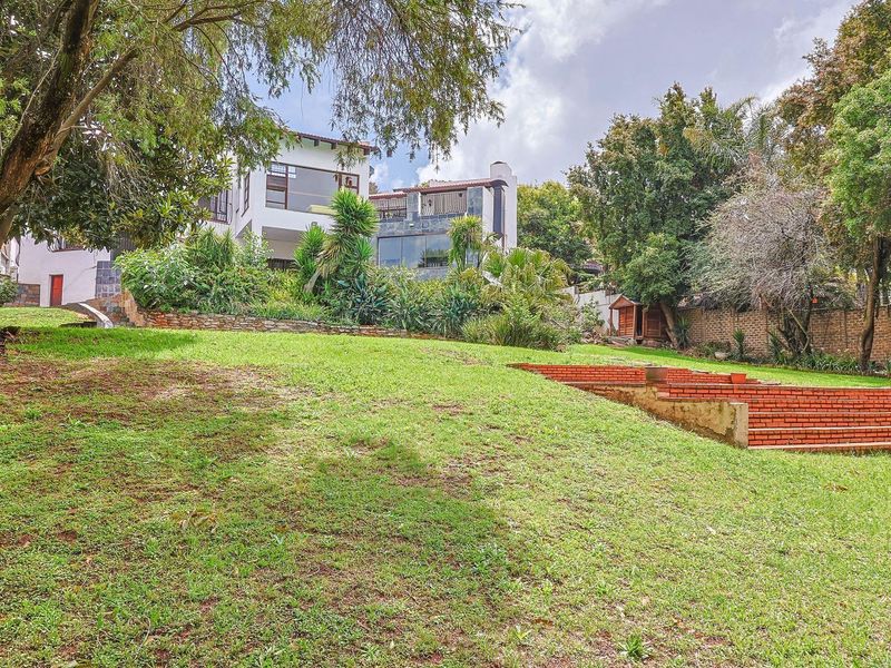 Spacious rear garden featuring tiered brick steps, established trees, and a view of the multi-level residential property facade.