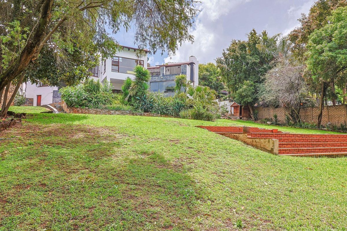 Spacious rear garden featuring tiered brick steps, established trees, and a view of the multi-level residential property facade.
