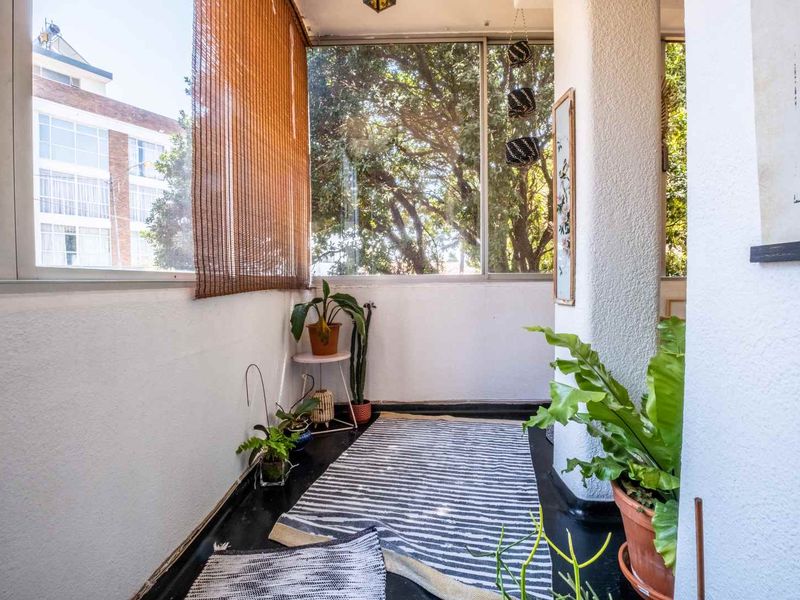 A sunlit enclosed balcony featuring large windows, a structural pillar, and a painted concrete floor, offering a bright and versatile outdoor space.