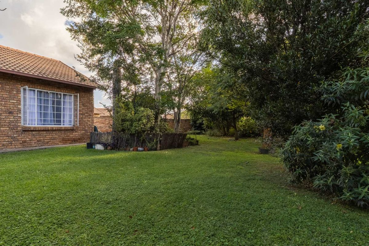 A view of the private rear garden featuring a lush lawn, mature trees, and the side elevation of the brick townhouse.