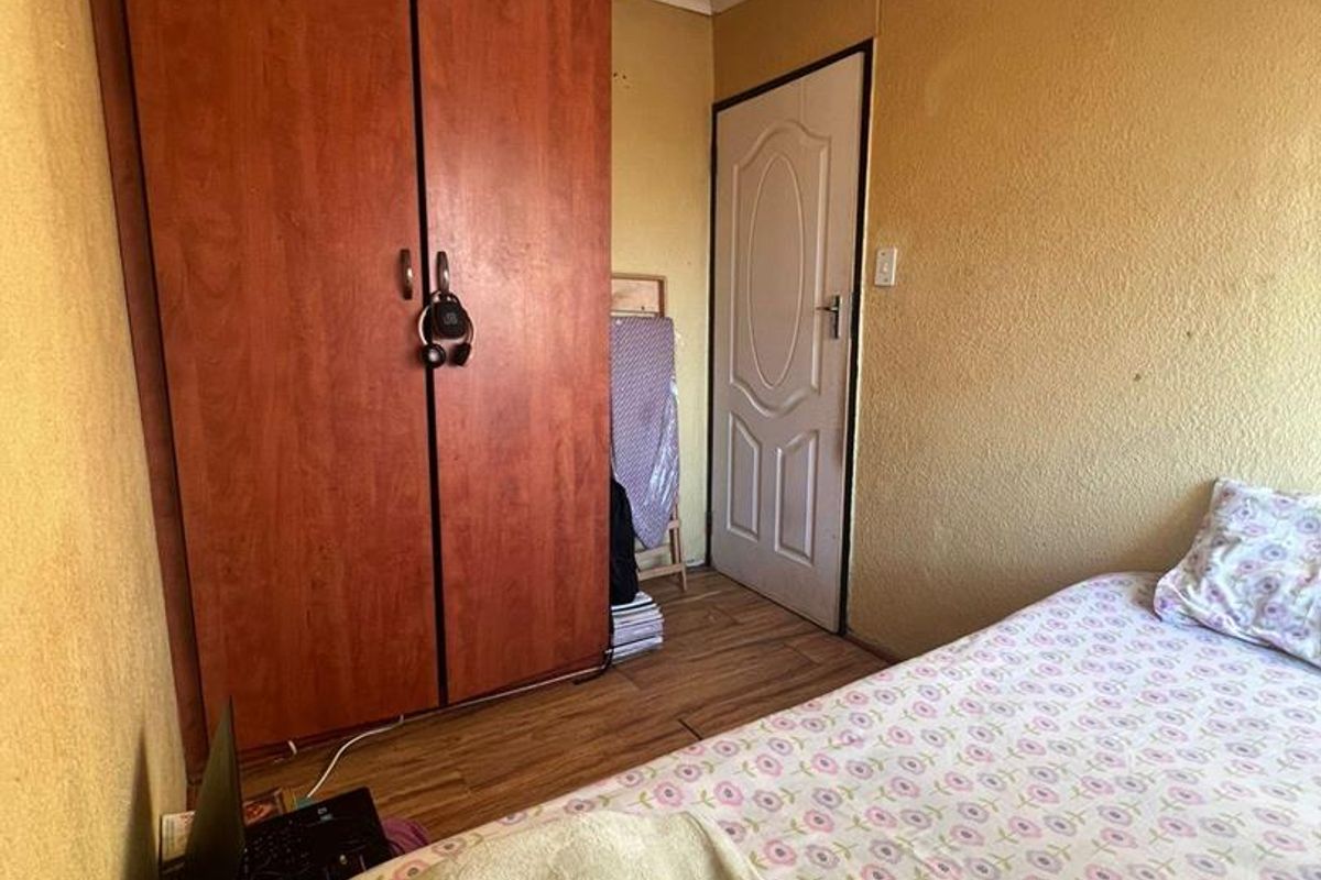 A compact bedroom featuring built-in wooden cabinetry, laminate flooring, and a standard interior door.