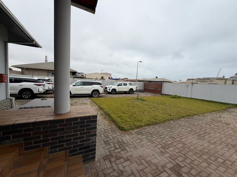 A paved rear courtyard area featuring a small lawn, boundary wall, and a covered patio space.