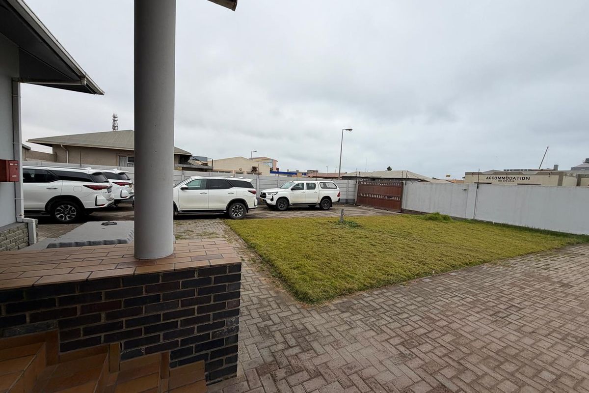 A paved rear courtyard area featuring a small lawn, boundary wall, and a covered patio space.