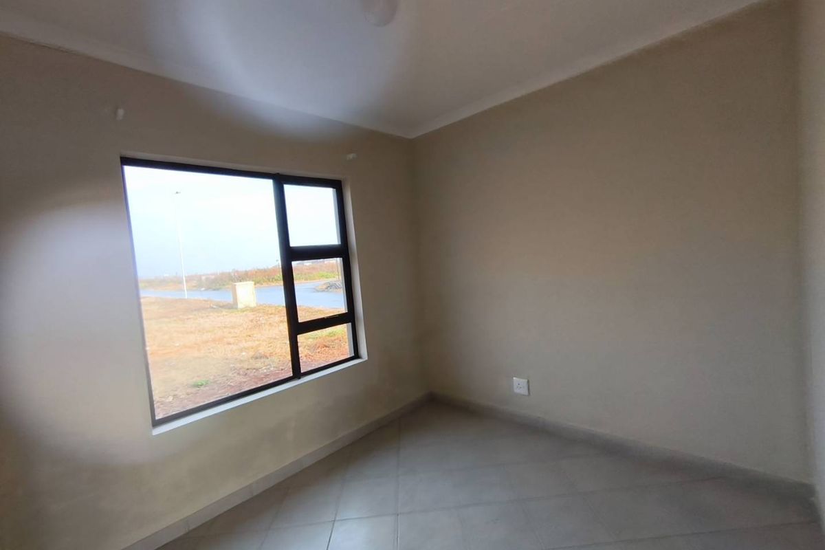 An empty bedroom featuring neutral wall paint, tiled flooring, and a large window offering an exterior view.