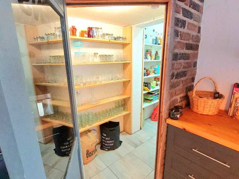 A functional scullery or pantry area featuring extensive built-in shelving, tiled flooring, and a rustic brick feature pillar with a timber countertop.