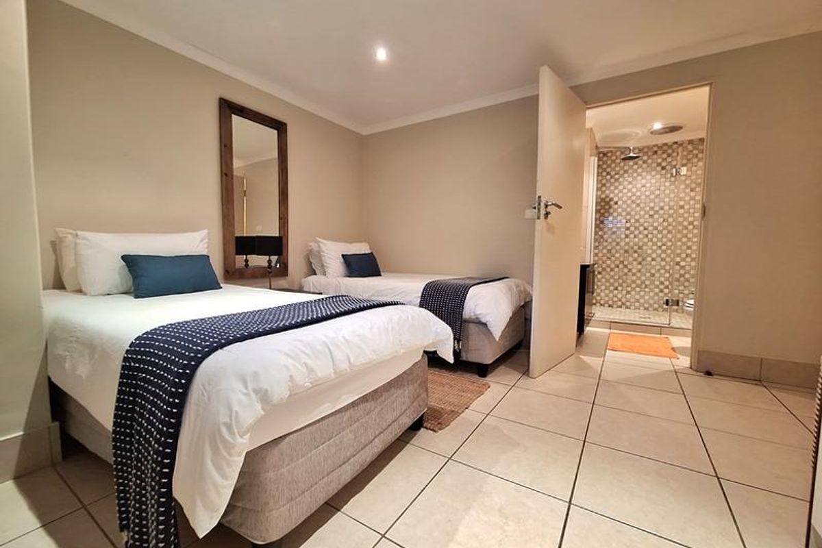 A well-maintained bedroom featuring tiled flooring, recessed ceiling lighting, and an en-suite bathroom with a glass-enclosed shower.