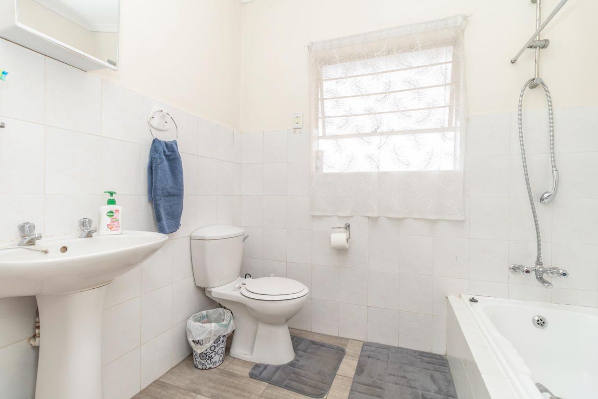 A functional bathroom featuring a pedestal basin, a standard toilet, and a shower-over-bath combination with white wall tiling.