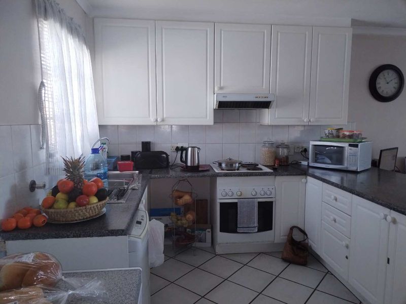 A functional kitchen featuring white cabinetry, granite countertops, tiled backsplash, and built-in appliances including an oven and extractor fan.