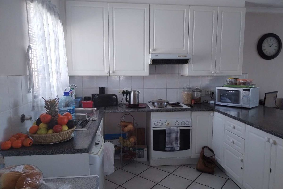 A functional kitchen featuring white cabinetry, granite countertops, tiled backsplash, and built-in appliances including an oven and extractor fan.