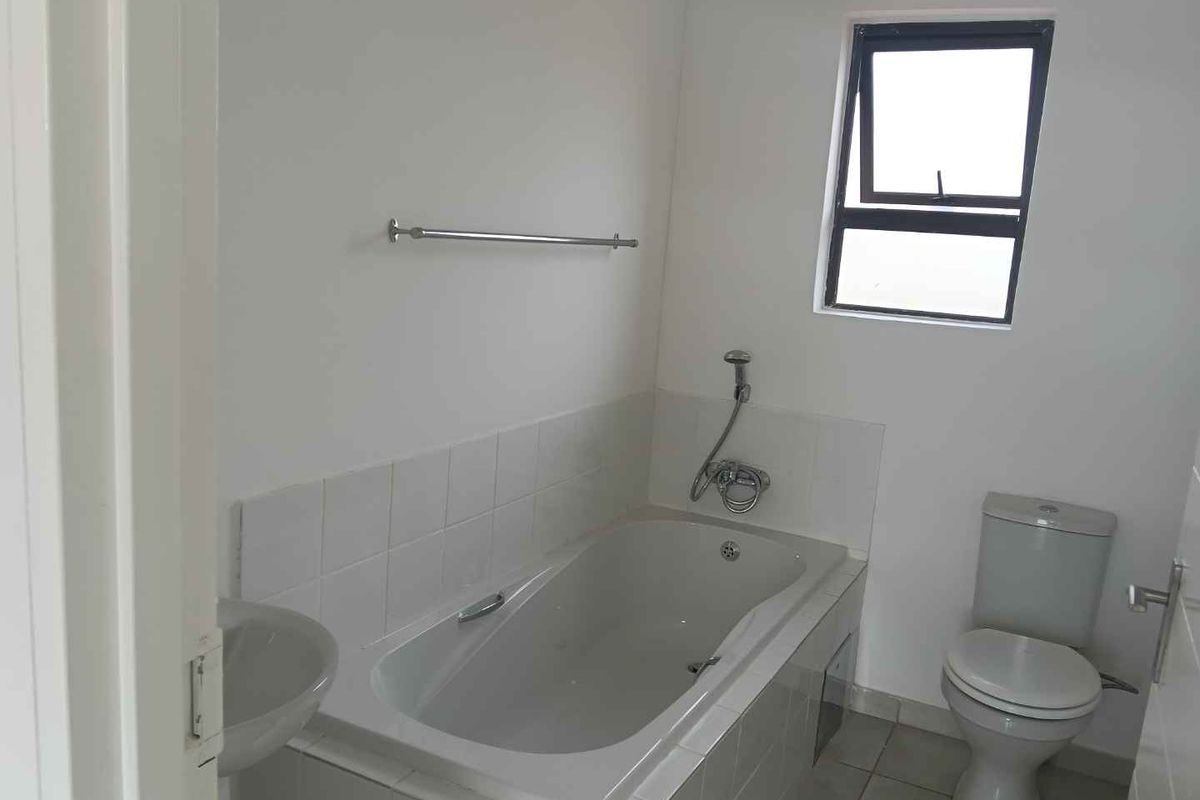 A functional bathroom featuring a built-in bathtub with shower mixer, a standard toilet, and a small wall-mounted basin.