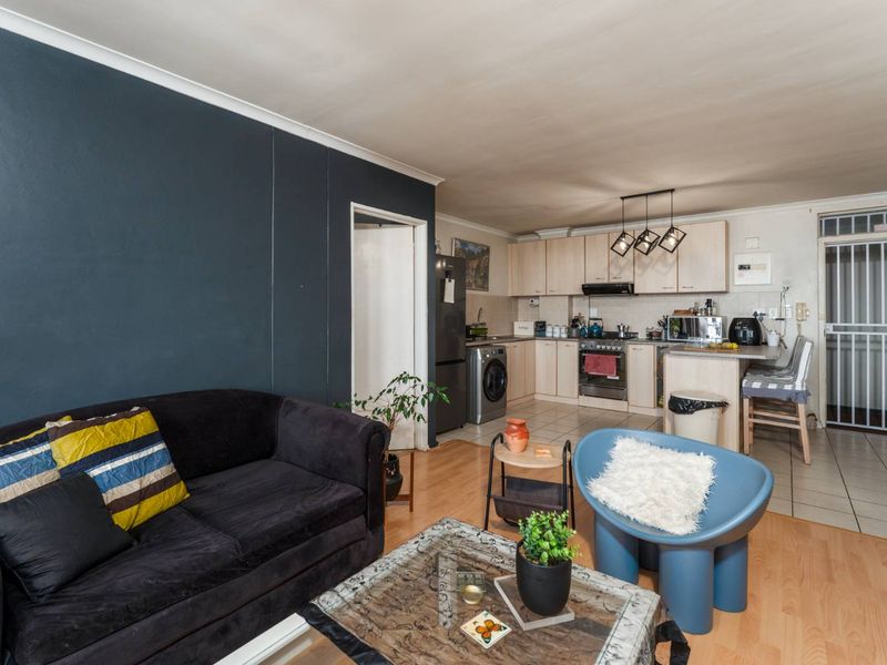 Open-plan living area featuring a kitchen with built-in cabinetry and stove, transitioning into a lounge space with laminate flooring and a security gate.