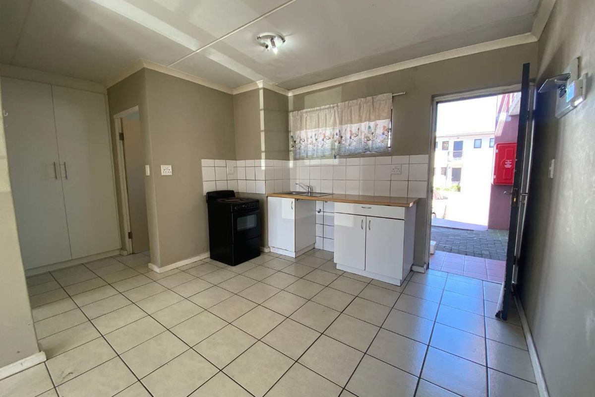 A functional kitchen area featuring tiled flooring, built-in cabinetry, a freestanding stove, and direct access to an exterior paved area.
