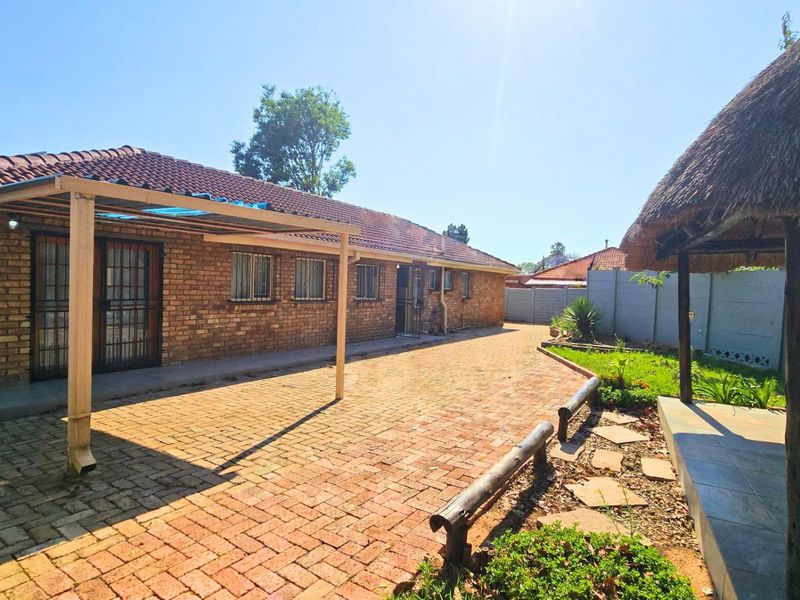 Rear exterior view featuring a brick house with a paved patio area and a traditional thatch lapa in the garden.