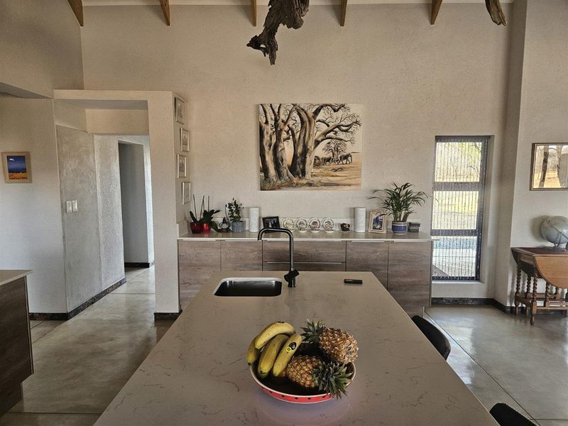 Modern kitchen featuring a central island with stone countertops, sleek cabinetry, polished concrete floors, and a high vaulted ceiling with exposed timber beams.