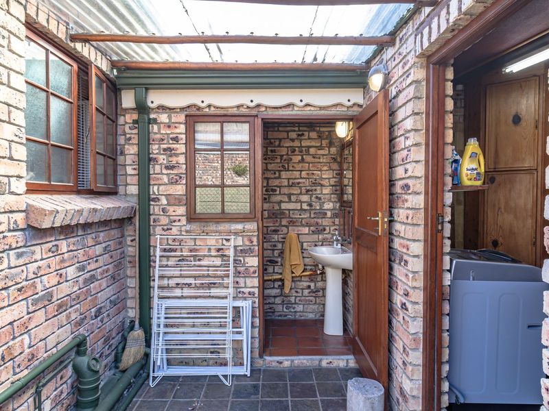 A functional outdoor utility area featuring exposed brick walls, a pedestal basin, and a translucent roof, providing a practical space for laundry or wash-up tasks.