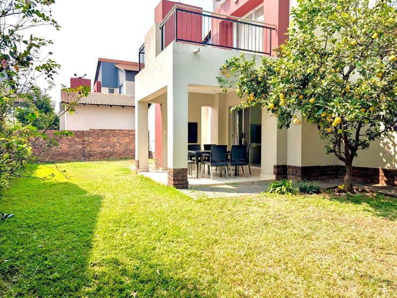 Rear view of the property featuring a covered patio, an upper-level balcony, and a well-maintained garden area with established trees.