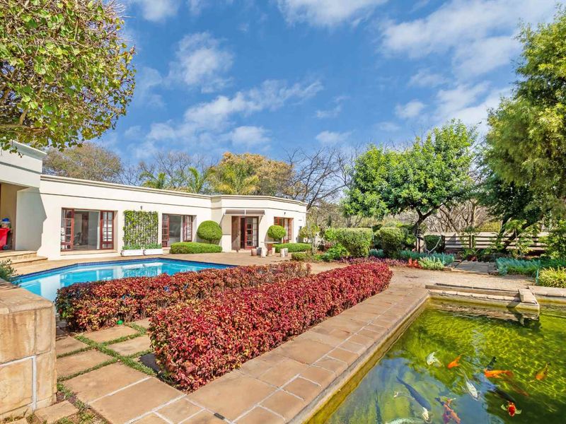 A beautifully landscaped outdoor area featuring a swimming pool, a large koi pond, and paved patio space with direct access to the home.