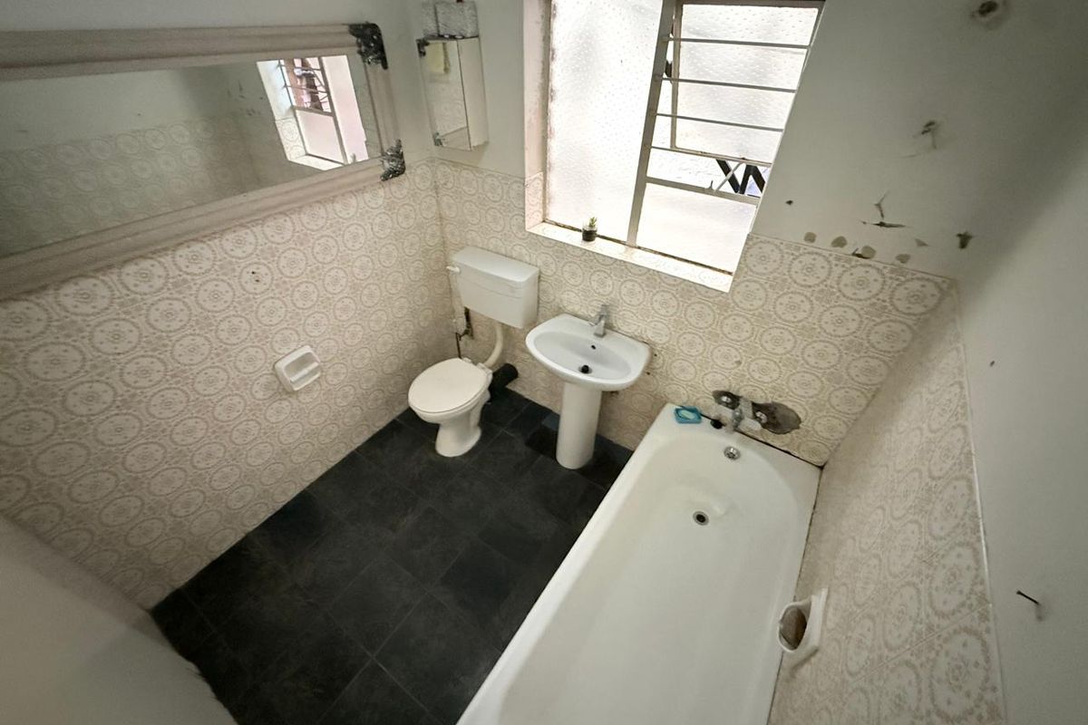 A dated bathroom featuring a bathtub, pedestal basin, and toilet with patterned wall tiles and dark floor tiles.