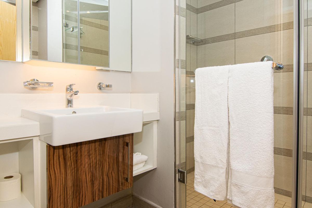 Modern bathroom featuring a vanity with wood-grain cabinetry, a ceramic basin, and a glass-enclosed shower with neutral wall tiling.