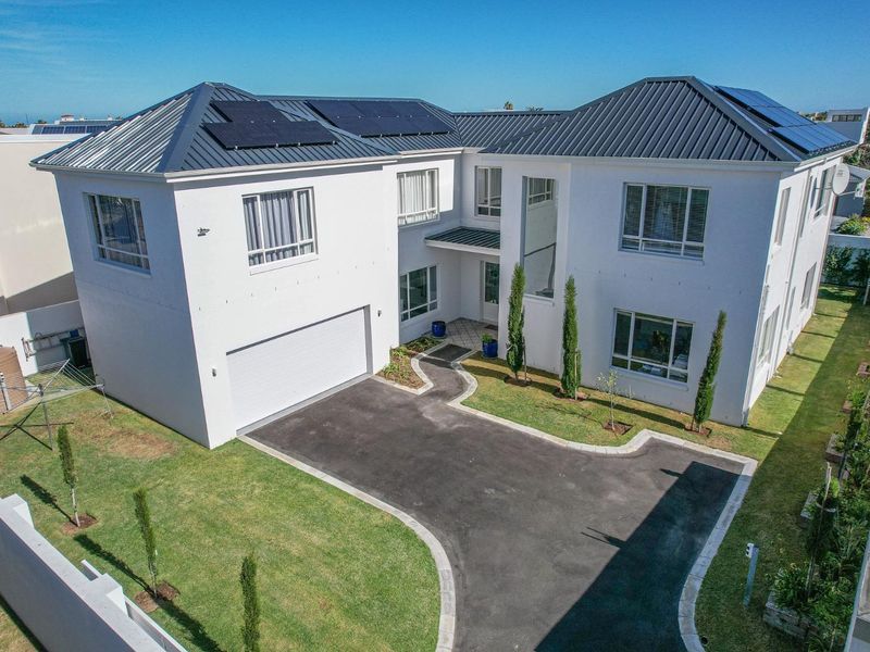 Aerial view of a modern two-story house featuring a metal roof with solar panels, a paved driveway, double garage, and a well-maintained front garden.