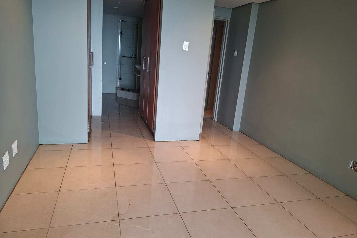 An empty bedroom featuring tiled flooring, built-in wooden cupboards, and an en-suite bathroom access point.