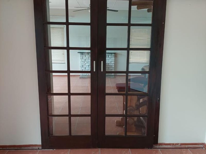 A transition space featuring dark timber double french doors and terracotta-style ceramic floor tiles, currently vacant with missing skirting boards.