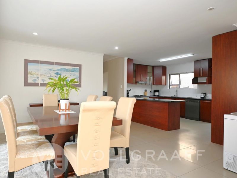 Spacious open-plan living and dining area featuring a modern kitchen with dark wood cabinetry, a central island, and tiled flooring throughout.