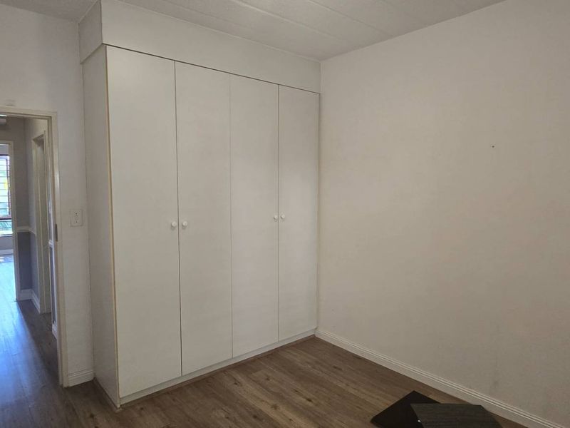 A clean, empty bedroom featuring built-in cupboards and modern laminate flooring, offering a neutral canvas for personalization.
