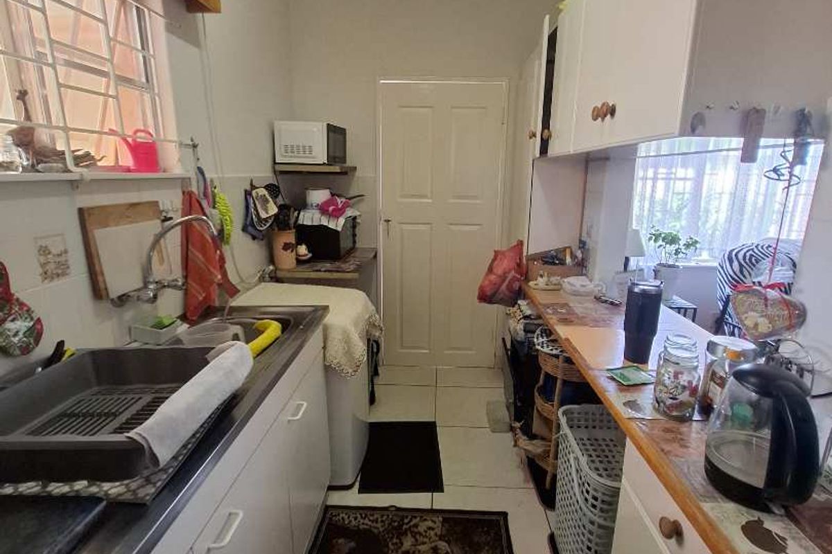 A compact galley-style kitchen featuring white cabinetry, tiled flooring, and a stainless steel sink, offering a functional layout for meal preparation.