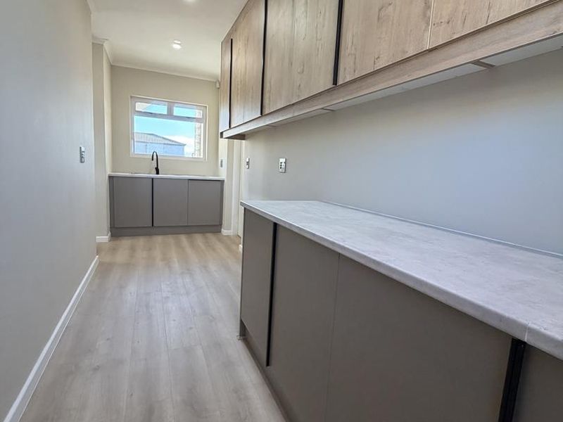 A modern, clean scullery featuring ample built-in cabinetry, laminate countertops, and neutral finishes, providing a functional and organized secondary kitchen or utility space.