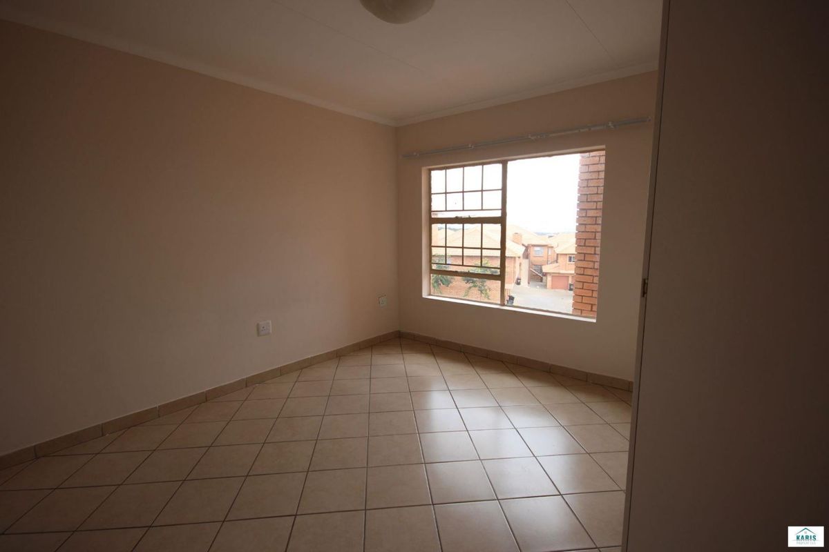 A bright, empty bedroom featuring neutral wall paint, tiled flooring, and a large window with a view of the surrounding complex.
