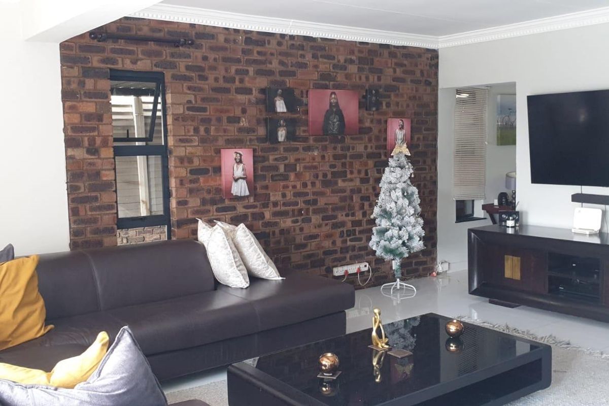 A living room featuring a prominent exposed brick feature wall, tiled flooring, and crown molding, creating a warm and textured living space.