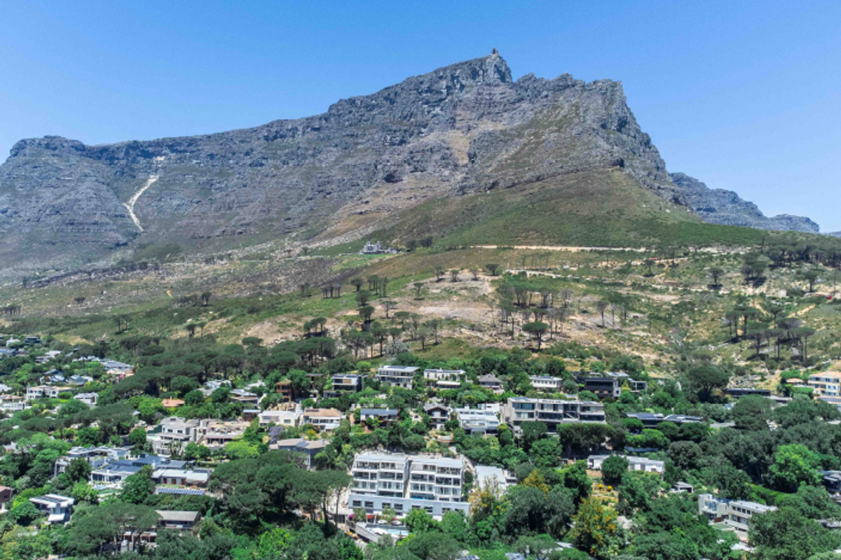 An elevated aerial view showcasing the property nestled within a lush, green residential neighborhood against the backdrop of a prominent mountain range.