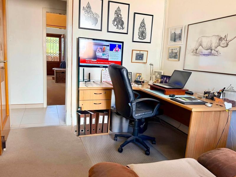 A functional home office space featuring a built-in desk, neutral wall finishes, and access to an adjoining hallway.