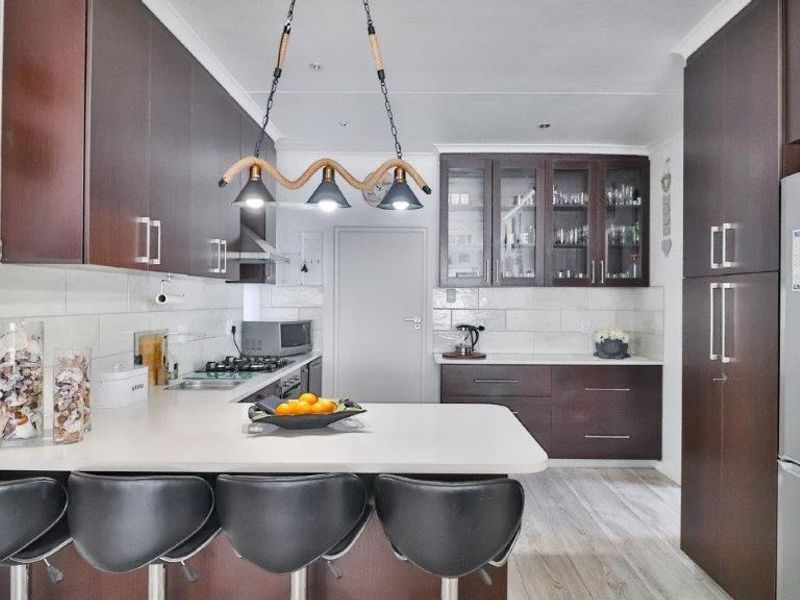 Modern kitchen featuring dark wood cabinetry, stone countertops, a gas hob, and a breakfast bar with integrated lighting.