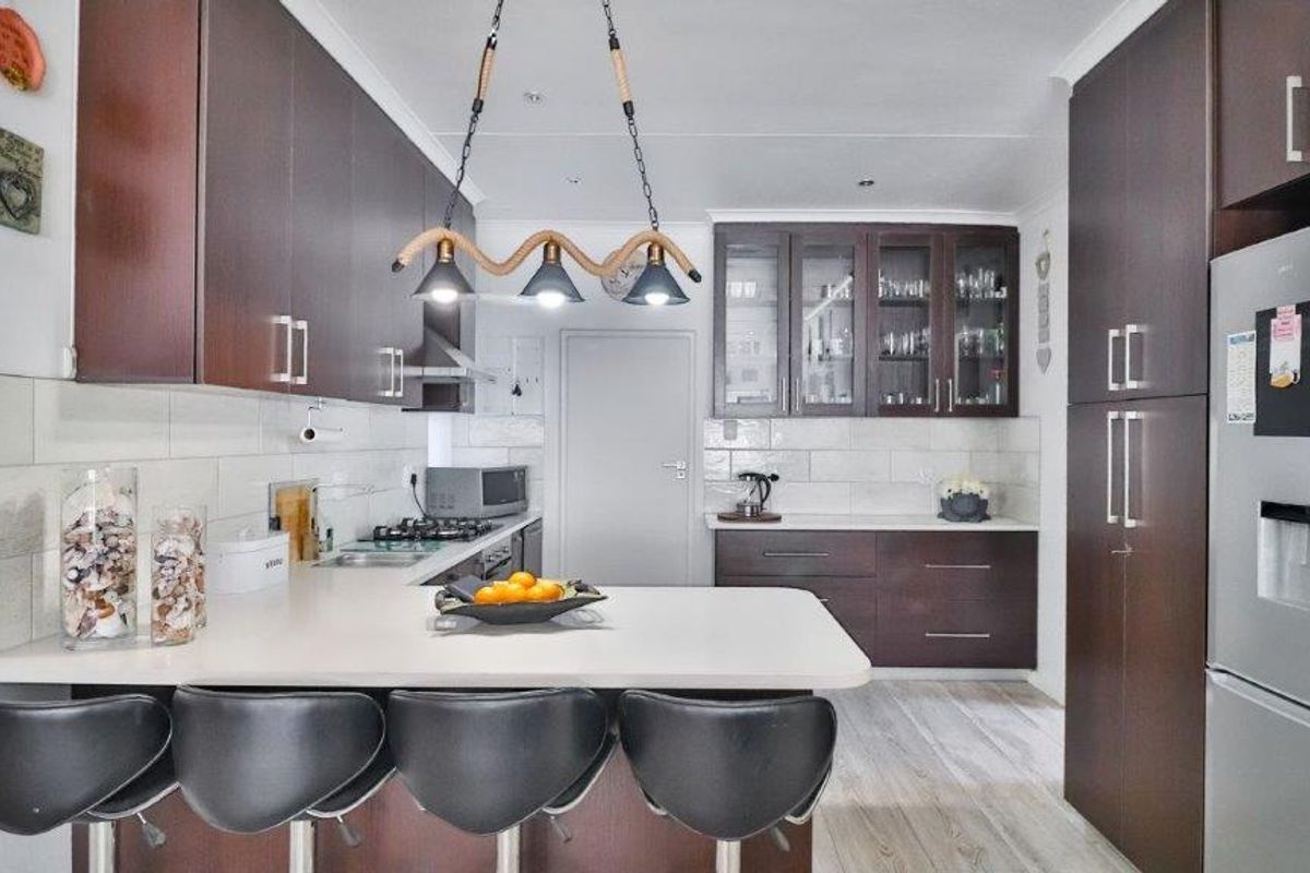 Modern kitchen featuring dark wood cabinetry, stone countertops, a gas hob, and a breakfast bar with integrated lighting.